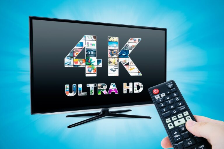 EnParlons.com - Écran TV moderne incurvé sur double pied noir affichant le texte '4K ULTRA HD' avec mosaïque d'images colorées intégrées dans les lettres, main tenant une télécommande noire avec bouton rouge allumé sur fond bleu turquoise dégradé, illustrant la qualité d'image Ultra HD 4K des abonnements IPTV Canada premium pour streaming haute définition avec télécommande pour contrôle facile des services de télévision IP